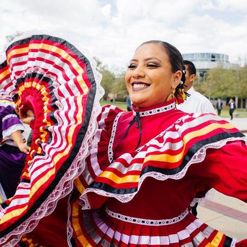 A young woman from the Chicano Student Programs performs a traditional Mexican folk dance in a brightly colored dress.