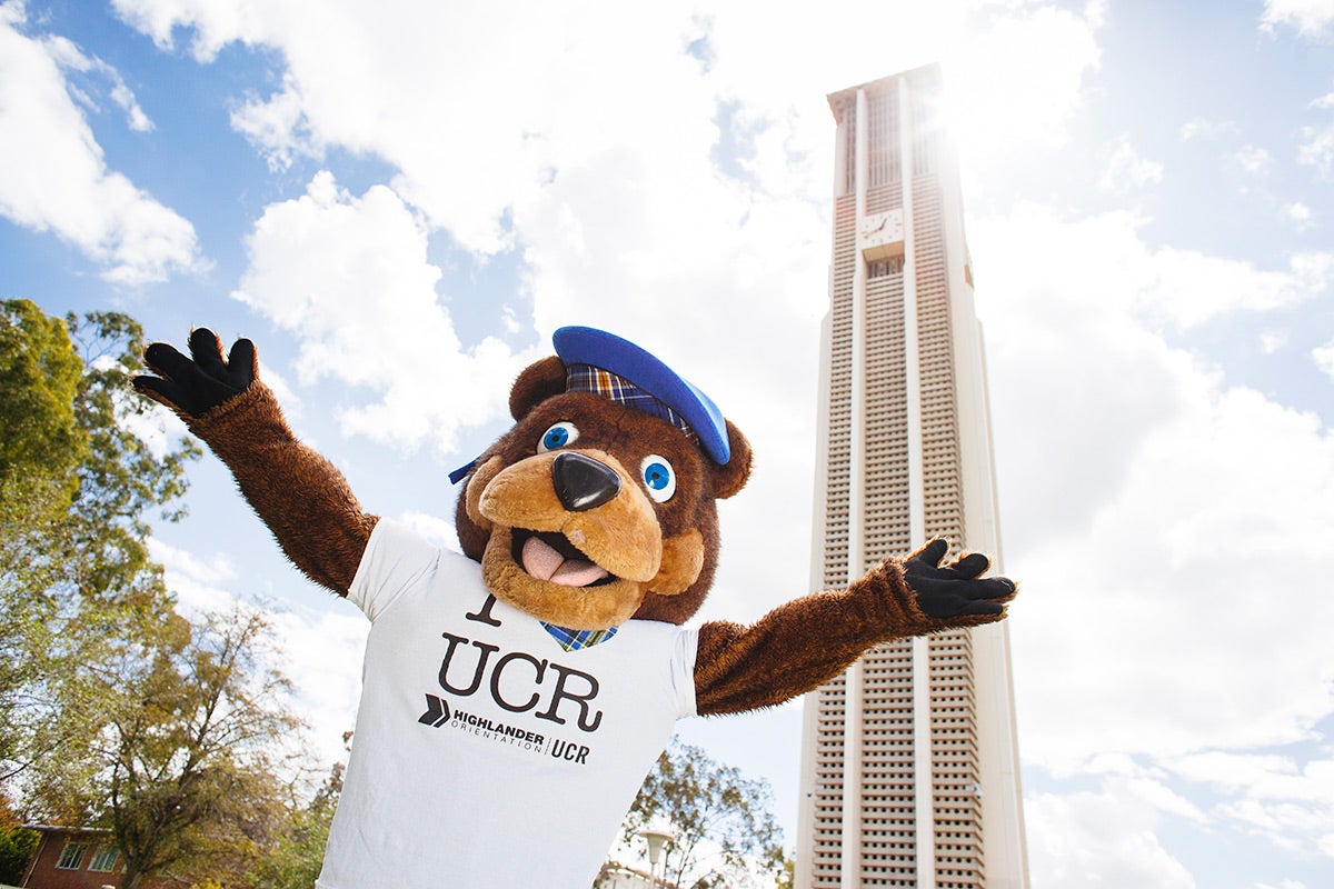 Scotty, the UCR mascot bear smiles with his arms spread wide in front of the UCR Bell Tower.