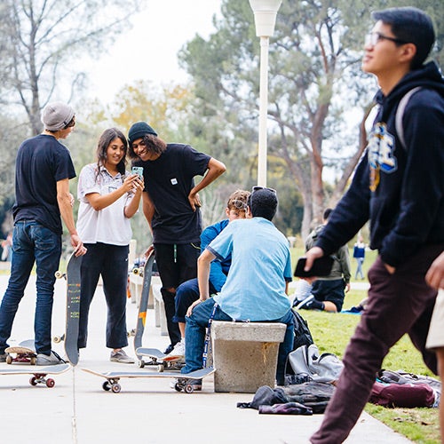 A group of UCR students with skateboards relax together on the UCR campus.